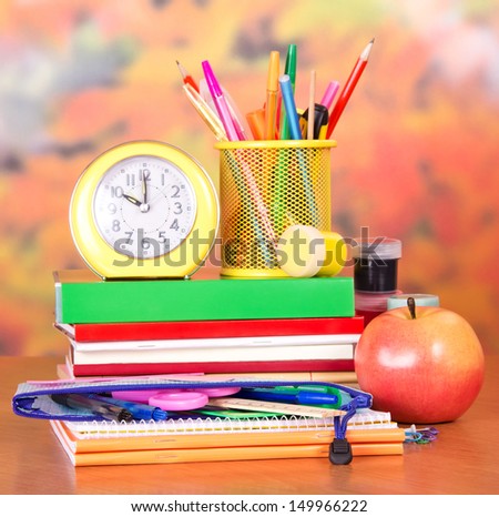 Books, alarm clock, a pencil-case with school accessories, paint and apple, on a table