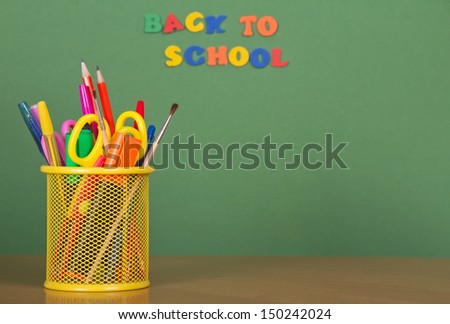 Back to school. Pencils, handles, scissors in a support, on a green background