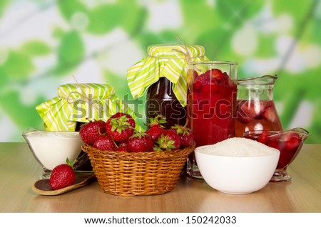 Jars of jam, a drink in a jug, cup with cream, basket with strawberry, cup with sugar and spoon on a table