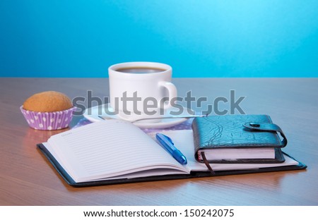 Open notepad the handle an organizer a cup of coffee and a cake on a table