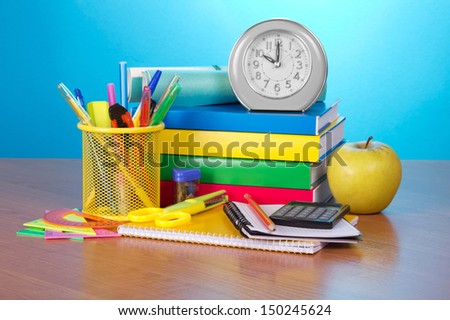 Pile of books, an exercise book, office supply, the calculator, an alarm clock and apple on a table