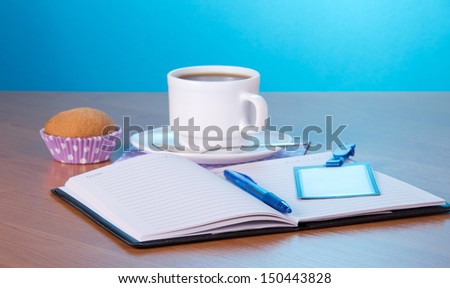 Open notepad the handle a badge a cup of coffee and a cake on a table