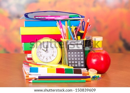 Books, alarm clock, pencil-case, a set of school accessories and an apple, on a table