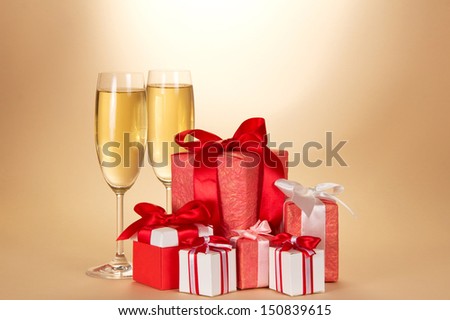 Two wine glass of champagne, set of gift boxes of various forms and coloring on a beige background