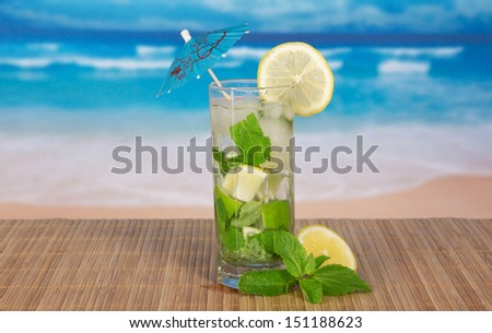 Green cocktail of alcohol with an umbrella, a lemon and spearmint, on a bamboo cloth against the sea