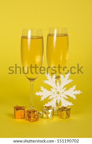 Christmas champagne in wine glasses small gift boxes and a snowflake on a yellow background