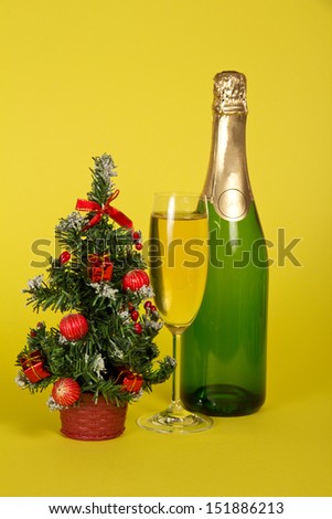 Bottle and wine glass with champagne, and a small fir-tree in a pot on a yellow background