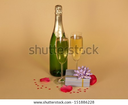 Bottle and two wine glasses of champagne a charming gift box, rose petals and small hearts on a beige background