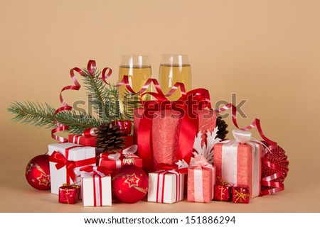 Gift boxes, Christmas toys, pine cones, serpentine and wine glasses with champagne on a beige background