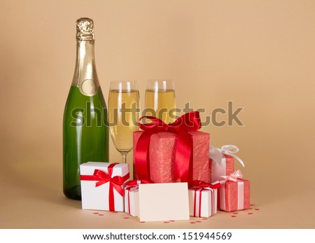 Bottle and wine glasses with champagne, gift boxes with a ribbon and a bow, and blank card on a beige background