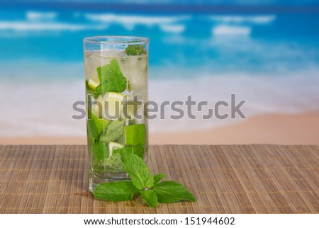 Green alcoholic cocktail from a citrus and mint, on a bamboo cloth against the sea