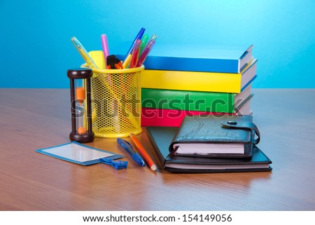 Organizer, notepad, books, blank badge, pens in a support, and hourglasses on a table