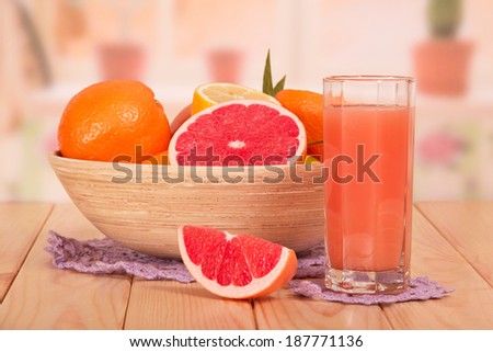 Glass of fresh juice and a bowl with different citrus fruits in the kitchen