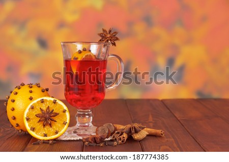 Cup of mulled wine on a wooden table with spices on a background of autumn leaves