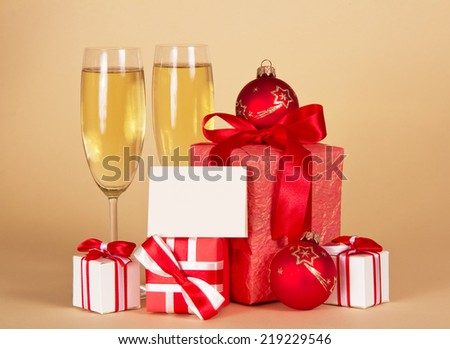 Wine glasses with champagne, Christmas gifts and toys and empty card for messages on a beige background