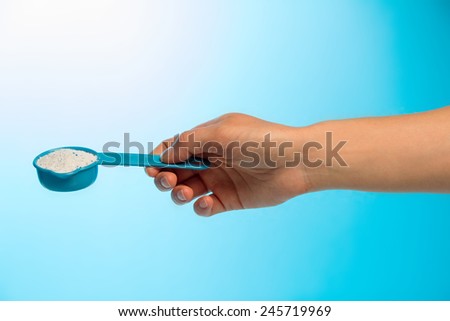 Washing powder in measuring cup in human hand on blue background