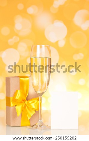 Champagne glass, gift and empty card on an abstract yellow background