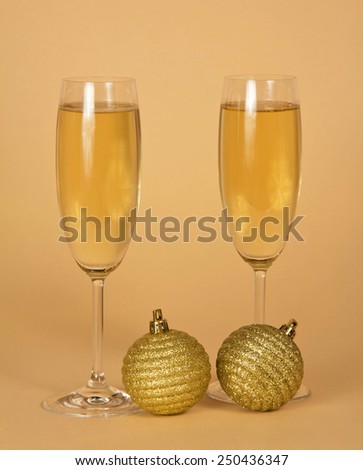 Two wine glasses with champagne and two golden New Year\'s balls on a beige background