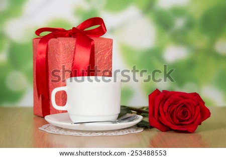 Cup of coffee and gift with a red rose on a table of cafe