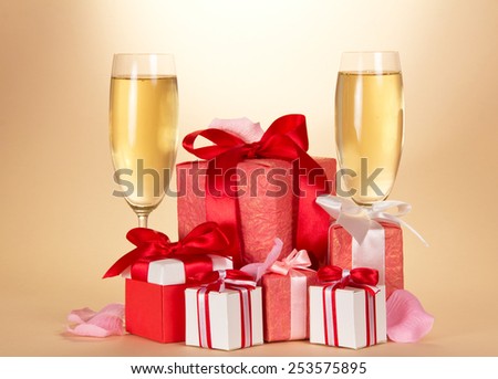 Two wine glass of champagne, set of gift boxes of various forms and coloring, and rose petals on a beige background