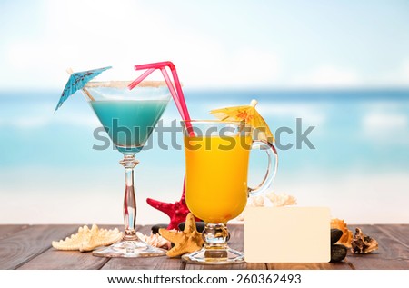 Cocktail with umbrella, blank card and juice on sea background