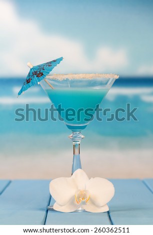 Cocktail with umbrella and flower on sea background