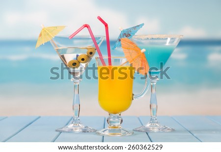 Three cocktails with umbrellas on sea background