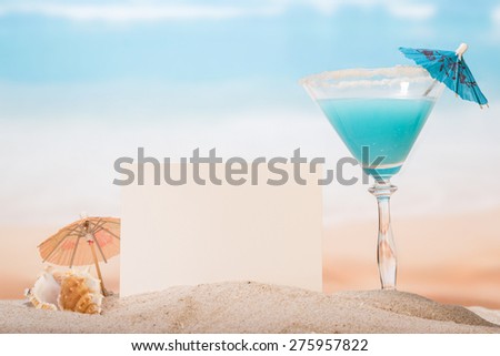 Cocktail with umbrella on sea beach with card background