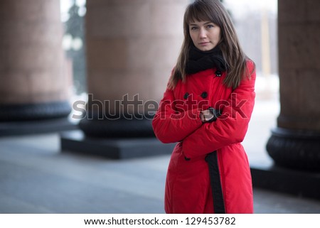 Beautiful girl in a red coat on the background of columns
