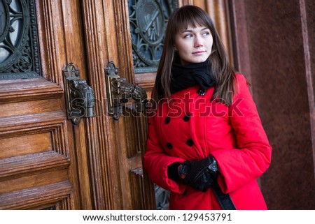 Beautiful woman in a red coat on the background of ancient doors