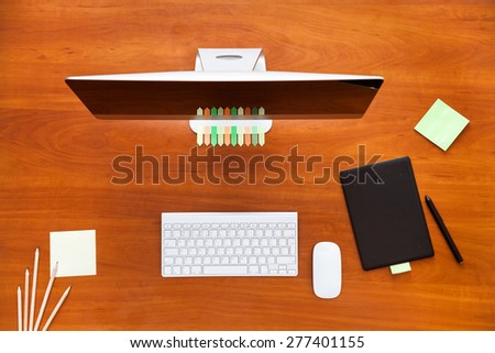 Brown wooden table, top view. On the table are, stationery items, stickers, keyboard, mouse, for convenient operation. Office mess.
