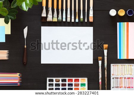 The ideal location of objects. Black table top view of the artist. On the table lay stationery items, paints, crayons, flowers, brushes, pencils and easy for creative work of the artist.