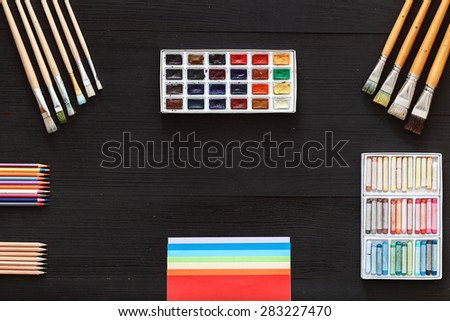 The ideal location of objects. Black table top view of the artist. On the table lay stationery items, paints, crayons, brushes, pencils and easy for creative work of the artist.
