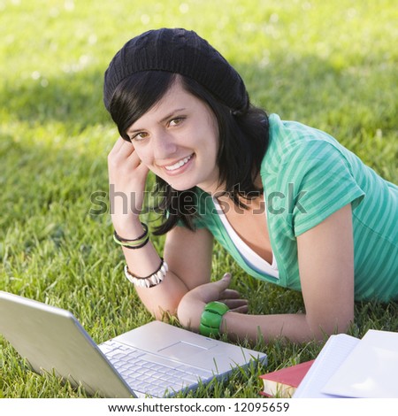 Teen studies with laptop in grass and smiles