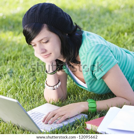 Teen studies with laptop in grass and smiles
