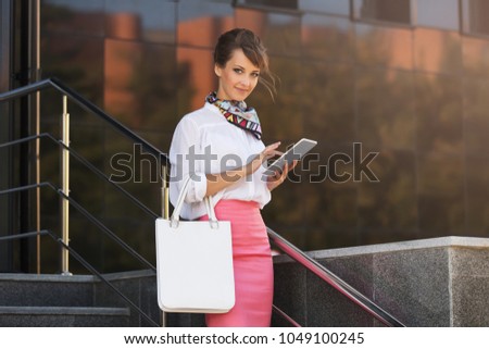 Young fashion business woman using digital tablet computer at office building. Stylish female model wearing white shirt and pink pencil skirt