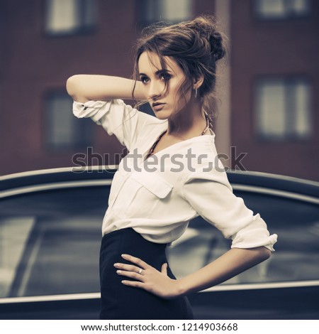 Young fashion business woman next to her car  Stylish female model with bun up do hair wearing white shirt and black pencil skirt