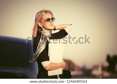 Fashion business woman with financial papers next to her car Stylish female model wearing black blazer and sunglasses outdoor