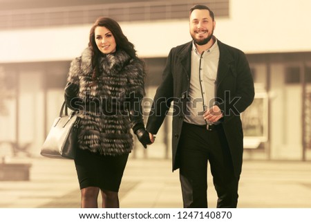 Happy young fashion couple walking on city street Stylish trendy man and woman wearing fox fur jacket and classic black coat