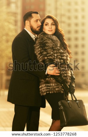 Happy young fashion couple in love walking on city street  Stylish trendy man and woman wearing fox fur jacket and classic black coat