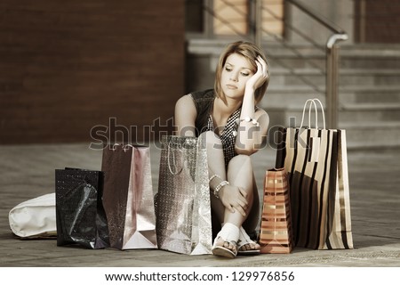 Sad young woman with shopping bags sitting on the sidewalk
