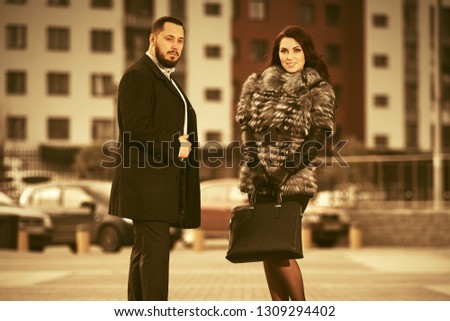 Happy young fashion couple in love walking on city street  Stylish trendy man and woman wearing fox fur jacket and classic black coat
