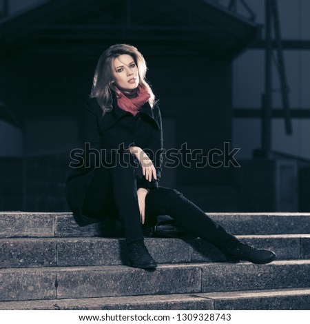 Fashion blond business woman sitting on steps Stylish female model in classic black coat