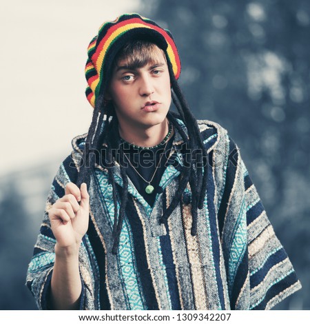 Sad young fashion hippie man walking outdoor Stylish trendy model wearing rasta hat and poncho