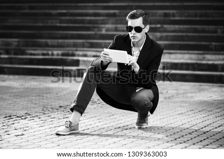 Young handsome business man using tablet computer on city street Stylish trendy male model wearing sunglasses and black suit jacket