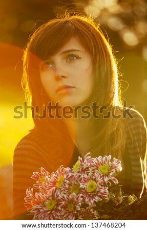 Sad young woman with a flowers by the sunset light