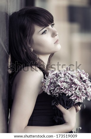Sad young woman with a flowers at the wall