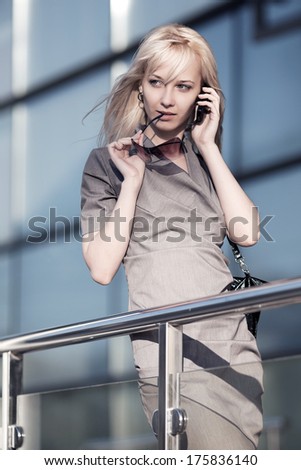Blond woman calling on the cell phone against office windows
