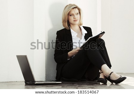 Young business woman with laptop sitting at the wall