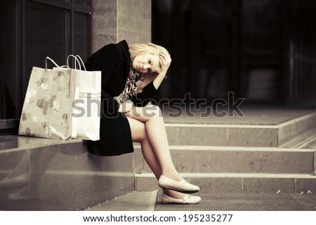Sad young woman with shopping bags at the mall window
